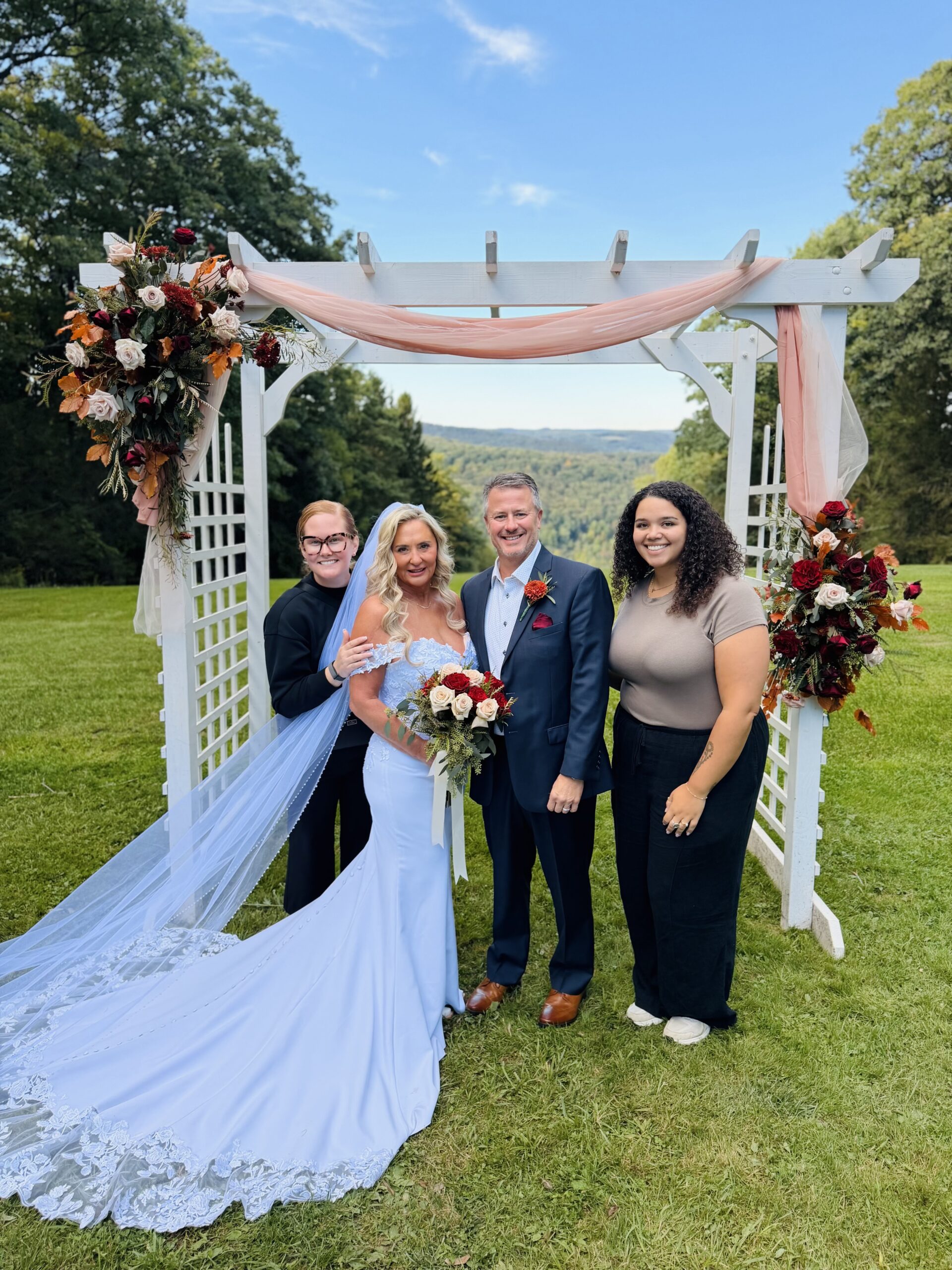 Paige Treadway and team with bride and groom celebrating under floral wedding arbor