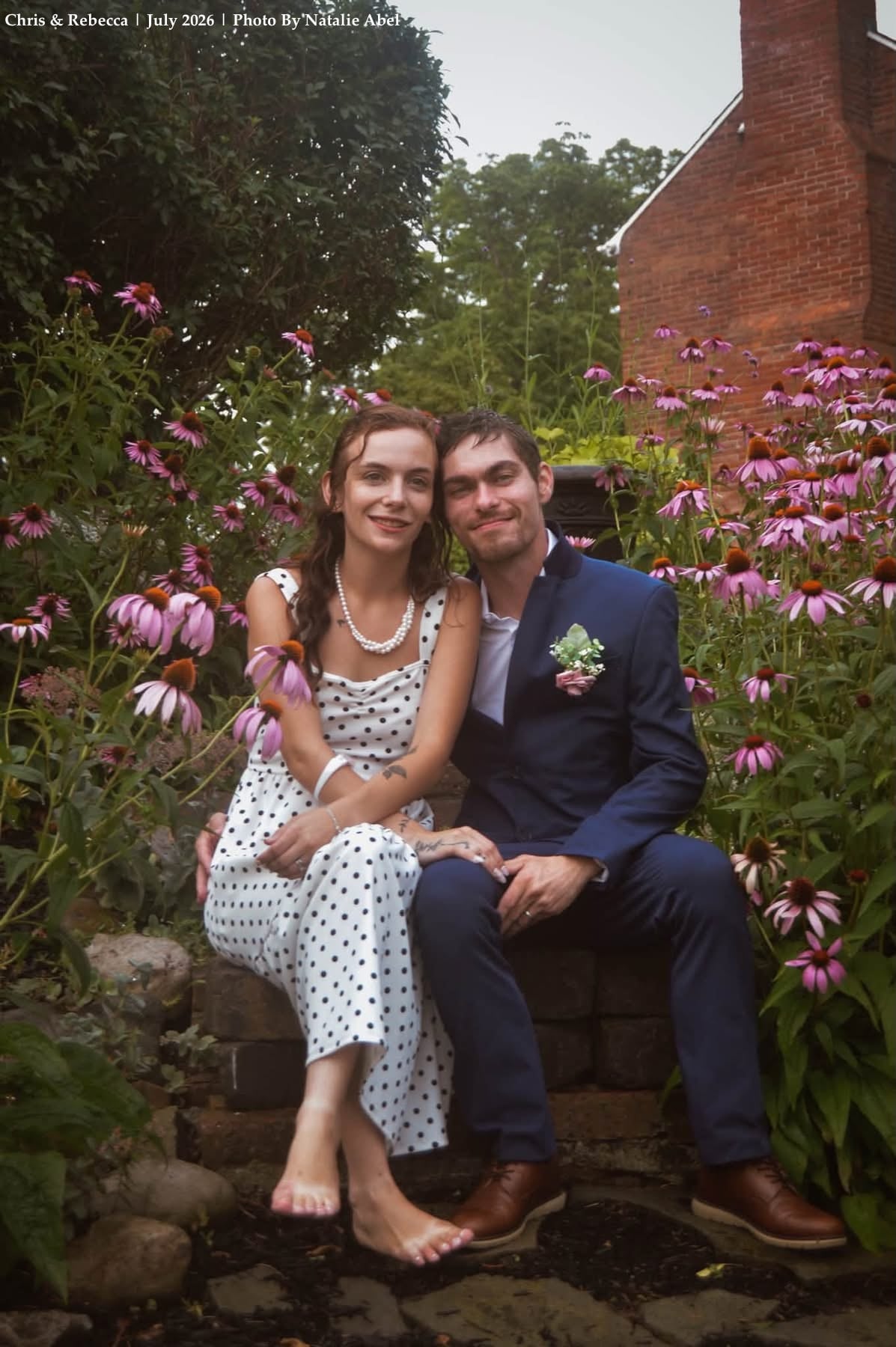 Paige and partner smiling together outdoors surrounded by summer wildflowers